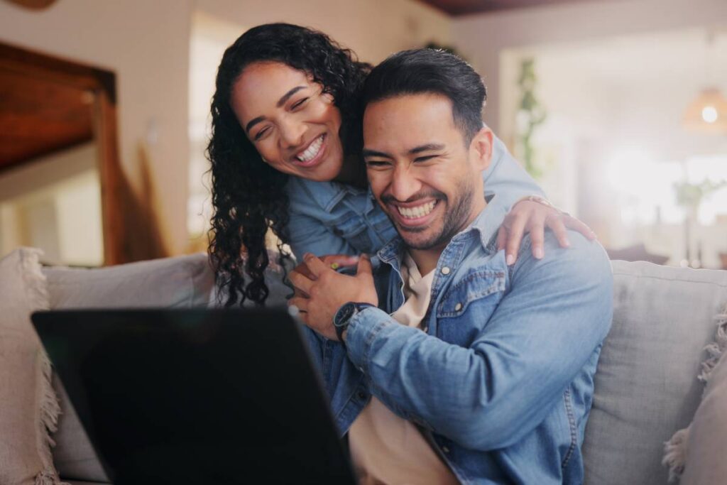 Smiling couple reviewing personal finance information together on a laptop to improve financial literacy.